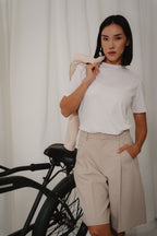 Woman in a white crew neck t-shirt and beige bermuda pants with single pleats at front, design for casual and office wear