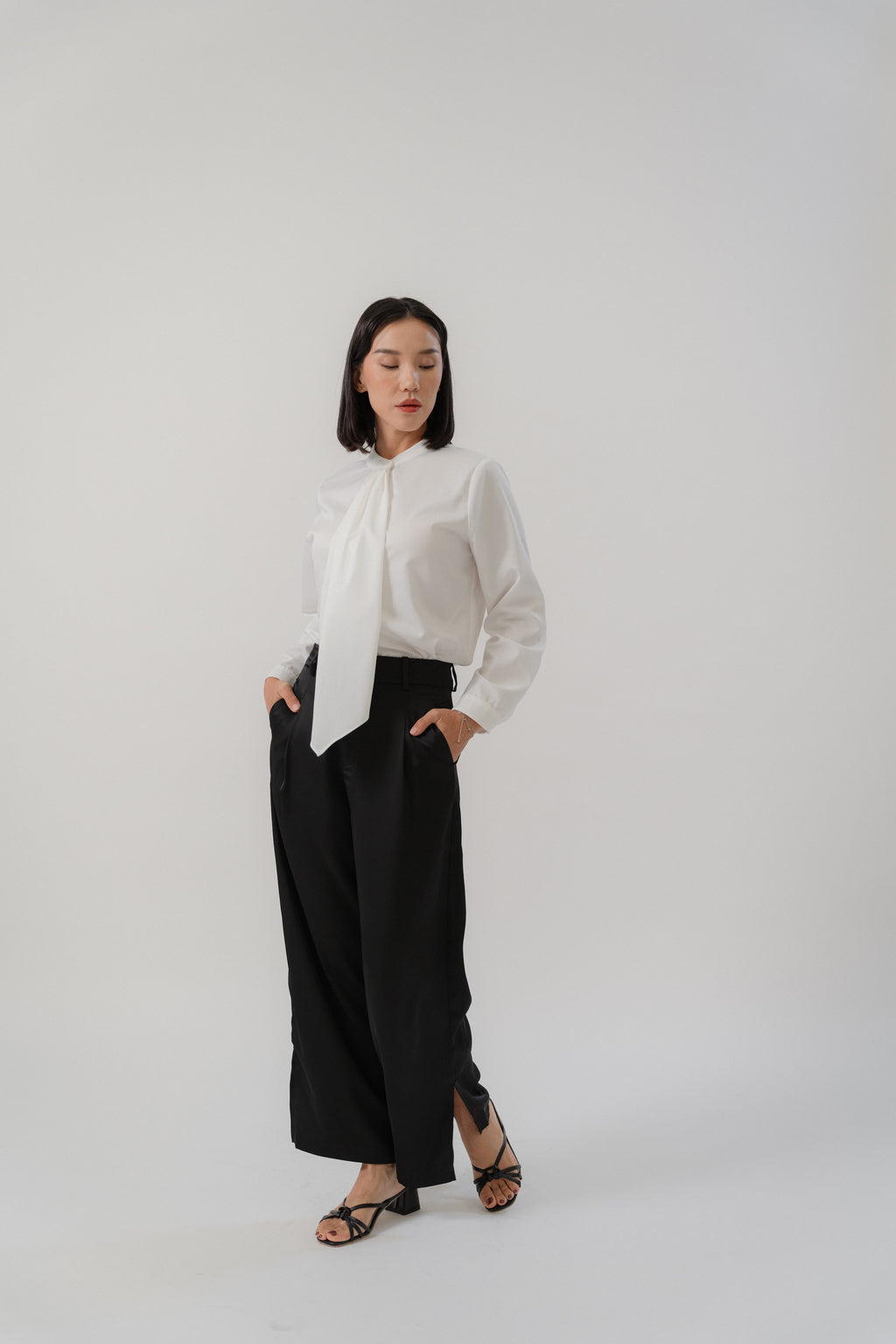 Woman wearing a white round neck tie blouse and black satin pants with modern silhouette, design for office daily wear