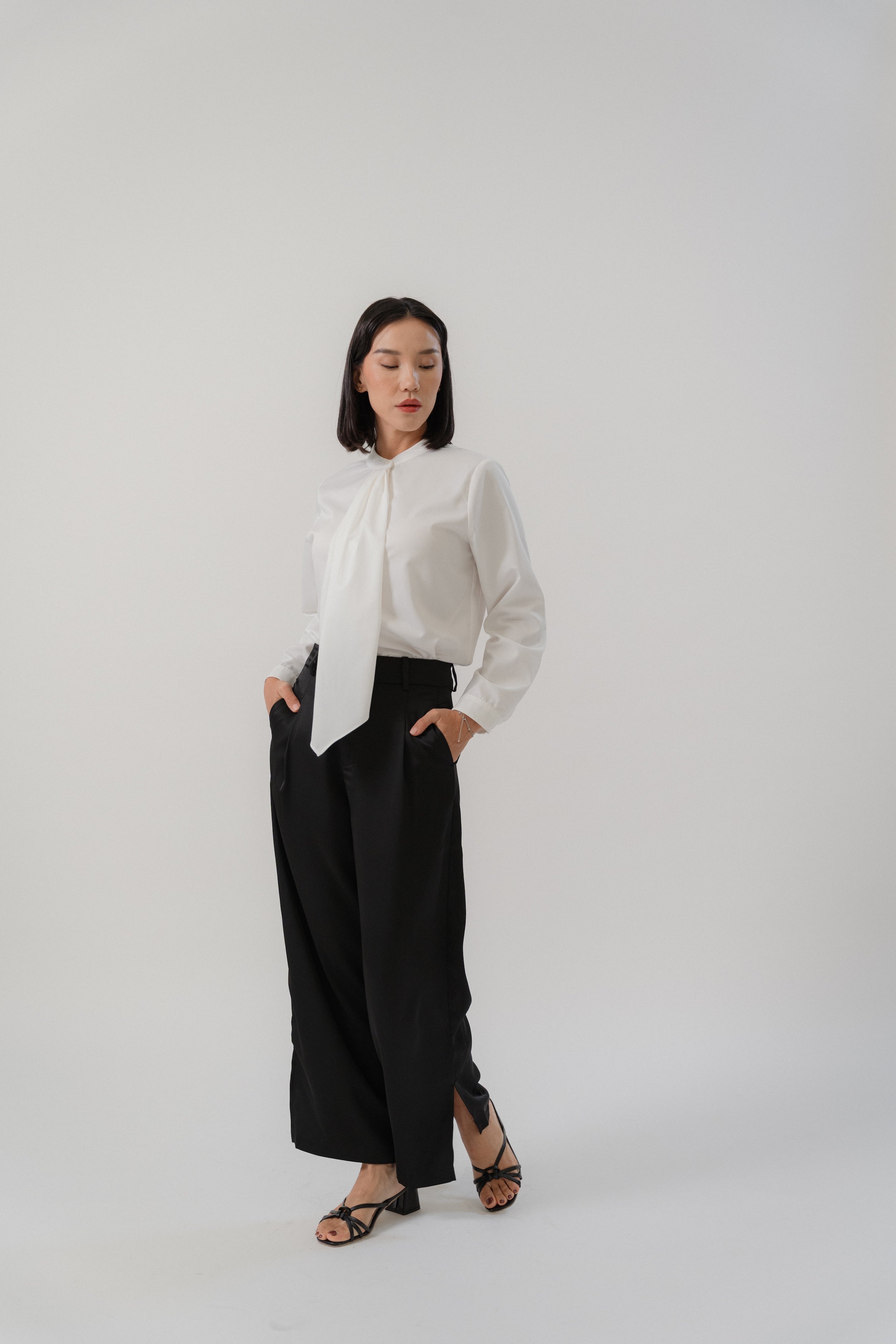 Woman wearing a white round neck tie blouse and black satin pants with modern silhouette, design for office daily wear