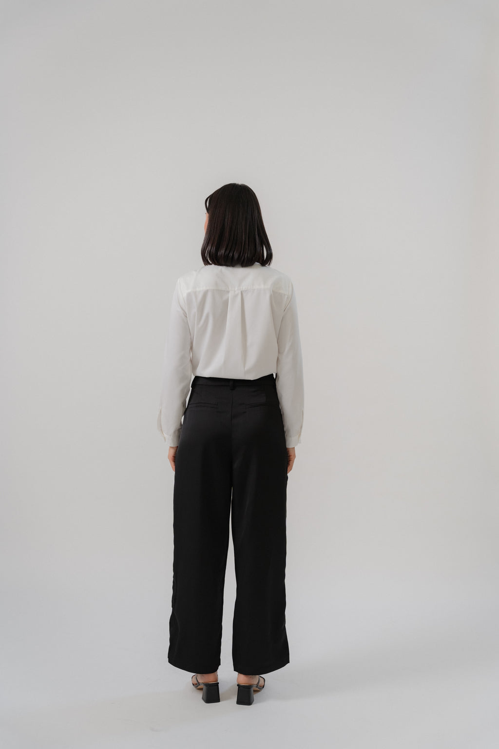 Woman wearing a white round neck tie blouse and black satin pants with modern silhouette, design for office daily wear