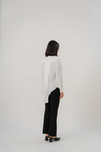 A woman wearing a white collared long-tailed blouse with puffy sleeves and a back pleated tail that creates a flowing silhouette, designed for office and city wear.