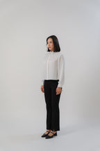 A woman wearing black bootcut pants and white collared long-tailed blouse with puffy sleeves and a back pleated tail that creates a flowing silhouette, designed for office and city wear.