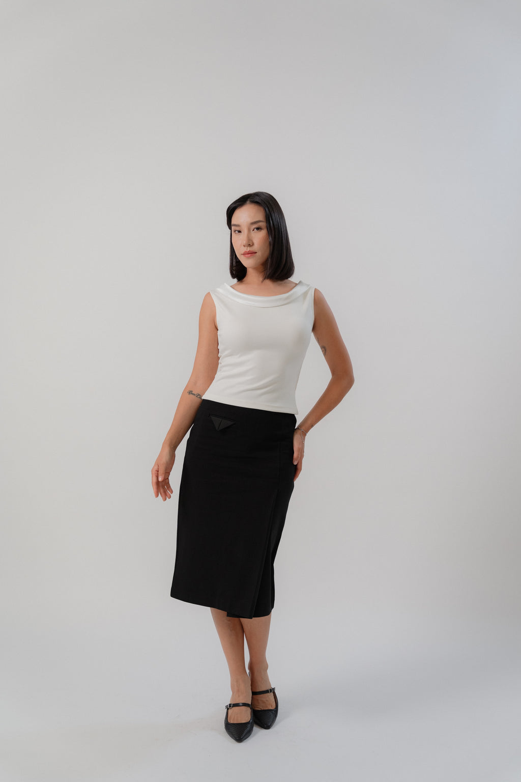 women wearing black slim skirt and white sleeveless top with boat neckline in satin, comfortable fit, designed for women's office and city wear.